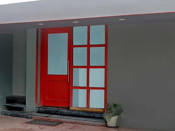 A red door with glass panels, a potted plant, and a small step leading to the entrance.