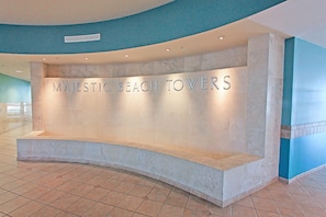 Ein Empfangsschalter mit der Aufschrift "MAJESTIC BEACH TOWERS" in einer modernen Lobby mit Fliesenboden und gewölbter Deckenkonstruktion.