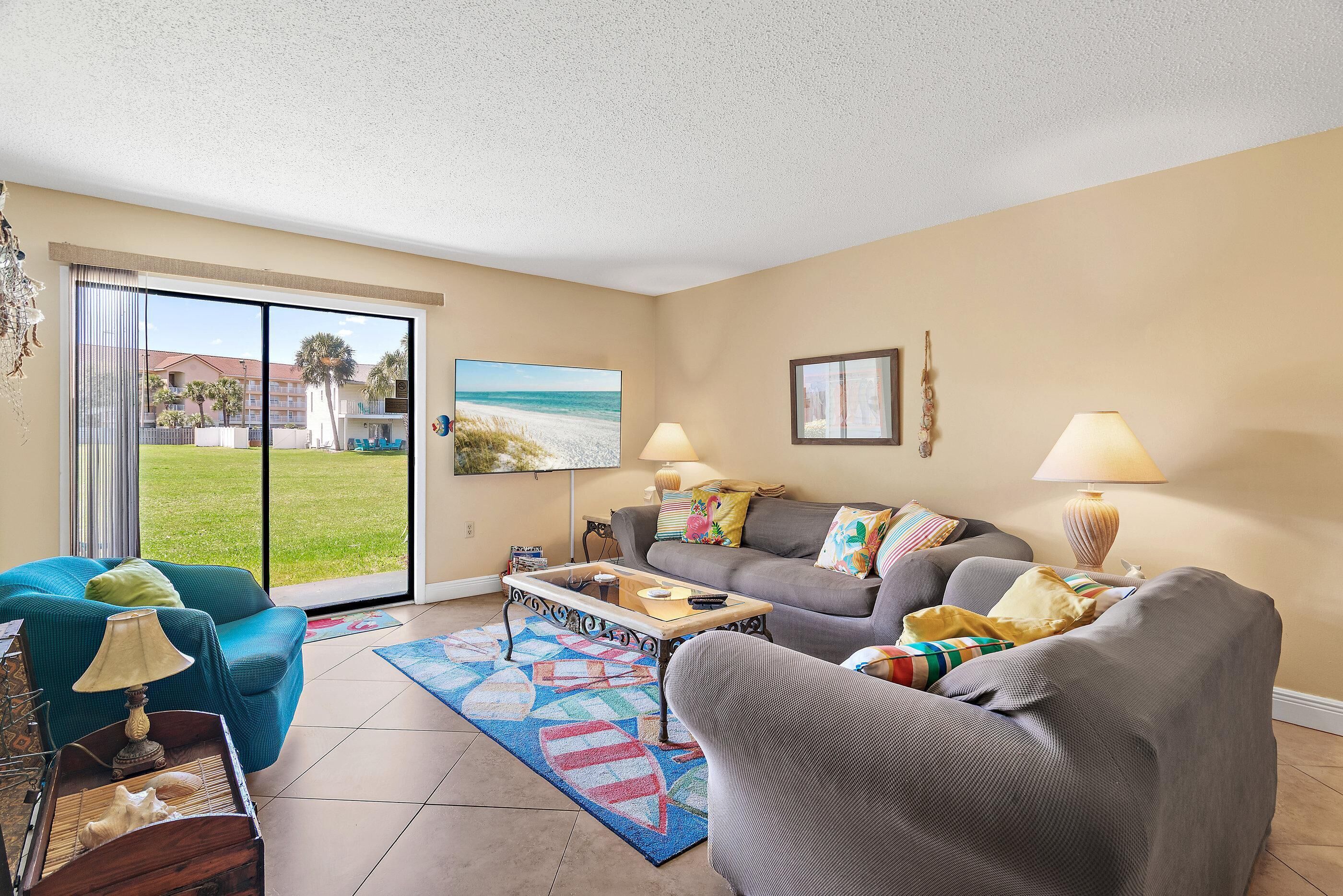 A living room with a sofa, armchair, coffee table, and a view of the beach through a sliding glass door.