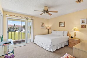 A hotel room with a bed, a nightstand with a lamp, a desk with a chair, a balcony with a view, and a ceiling fan. - Summerhouse Townhomes #2- Changes in Attitude (Miramar Beach)