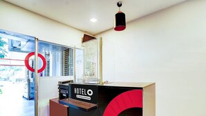 Een hotel receptiebalie met een 'HOTEL O' bord, een glazen toegangsdeur en een plafondlamp.