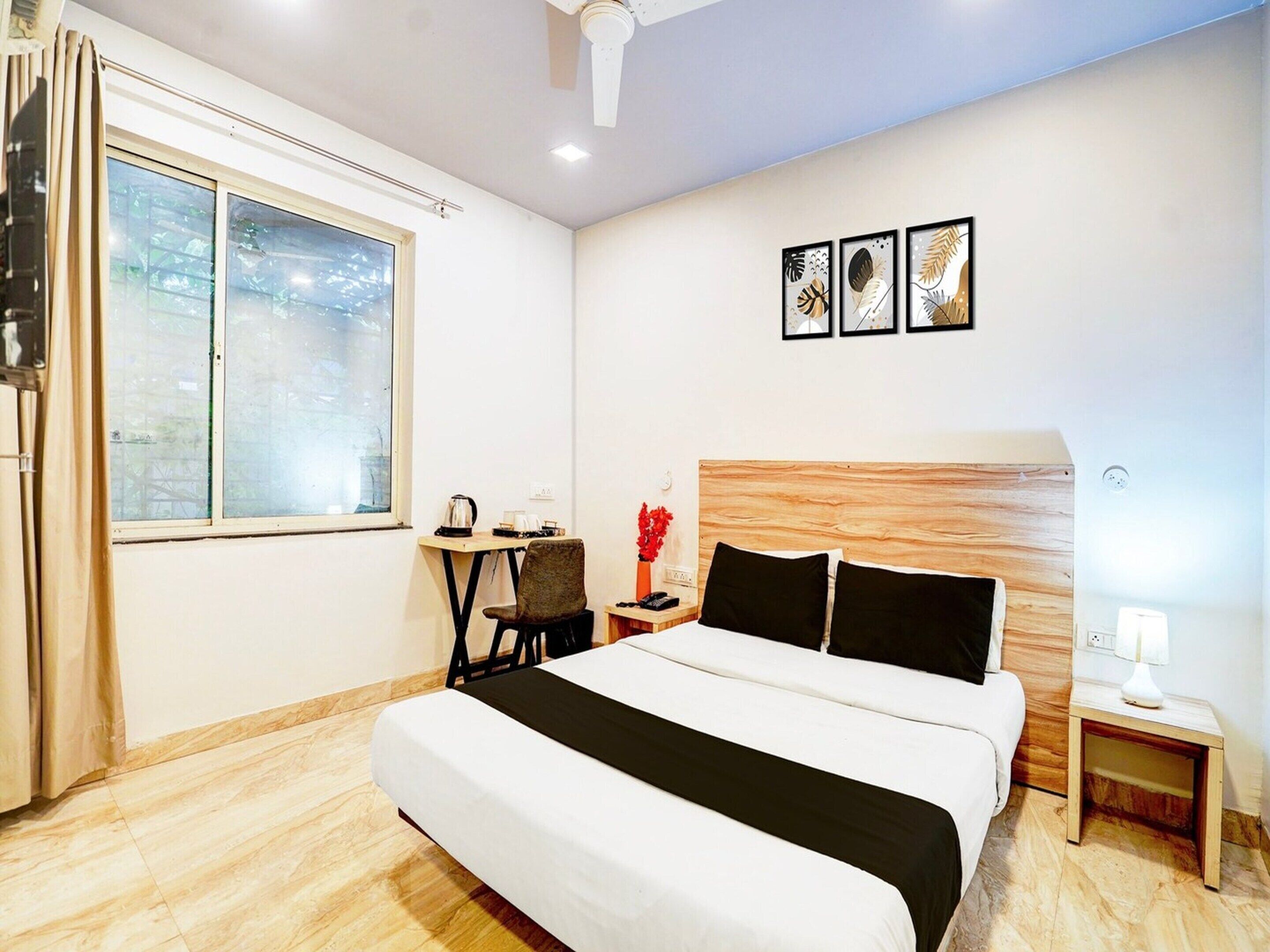 A hotel room with a bed, a small table, a chair, a nightstand, a lamp, and a window with curtains.