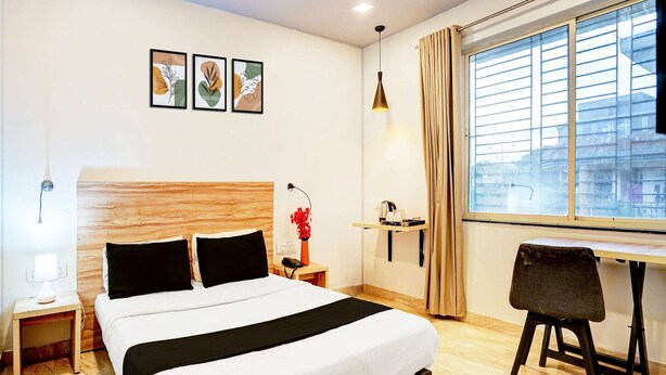 Een hotelkamer met een bed, nachtkastje, lamp, bureau, stoel, raam en kunst aan de muur.