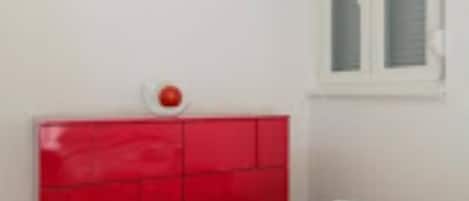 Una habitación con cabecera roja, una ventana con persianas y una cama con ropa de cama blanca.