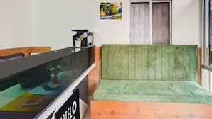 A hotel lobby with a reception desk, a green cushioned seating area, a window with a view, and a door.