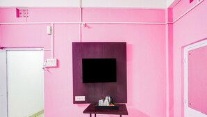 A room with pink walls, a mounted flat-screen TV, a small table with a tray, and a white door.
