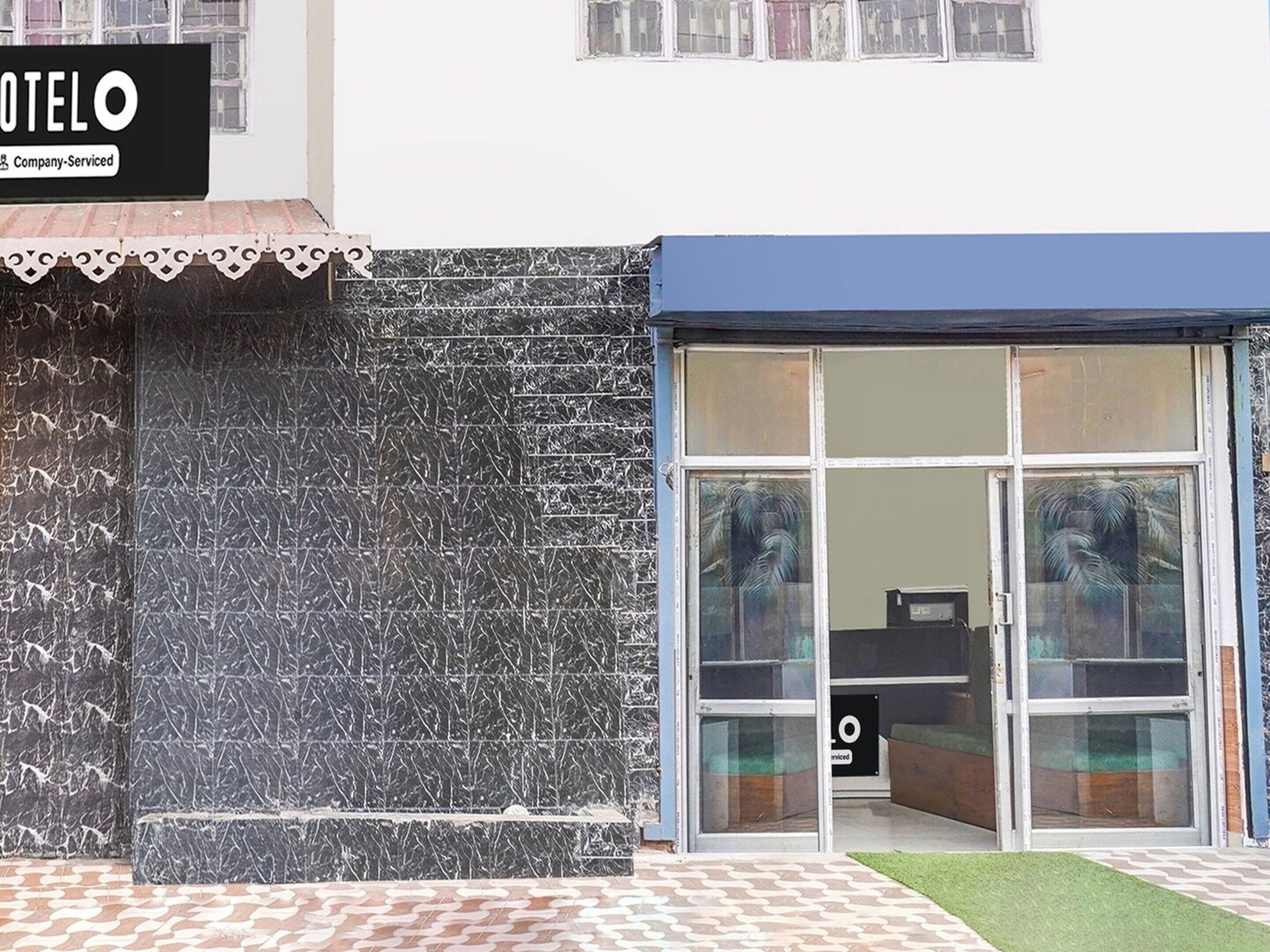 A hotel entrance with a tiled facade, a signboard, and a glass door leading inside.