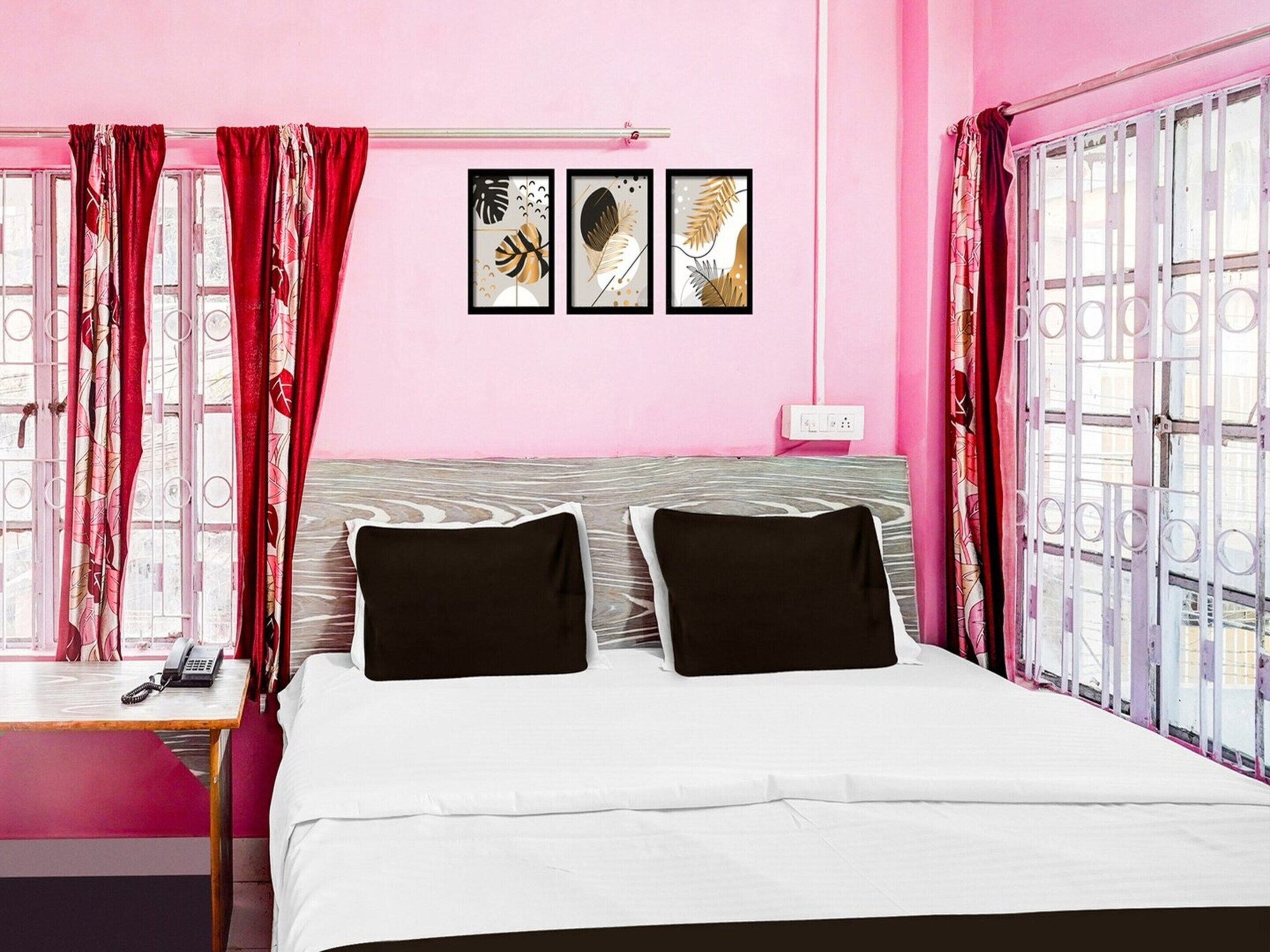 A pink-themed hotel room with a bed, a bedside table, a phone, and a window with curtains.
