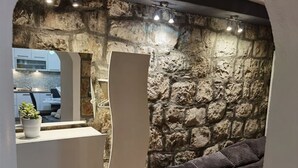 Une pièce aux murs de pierre, avec un lit, une petite table et une plante en pot.