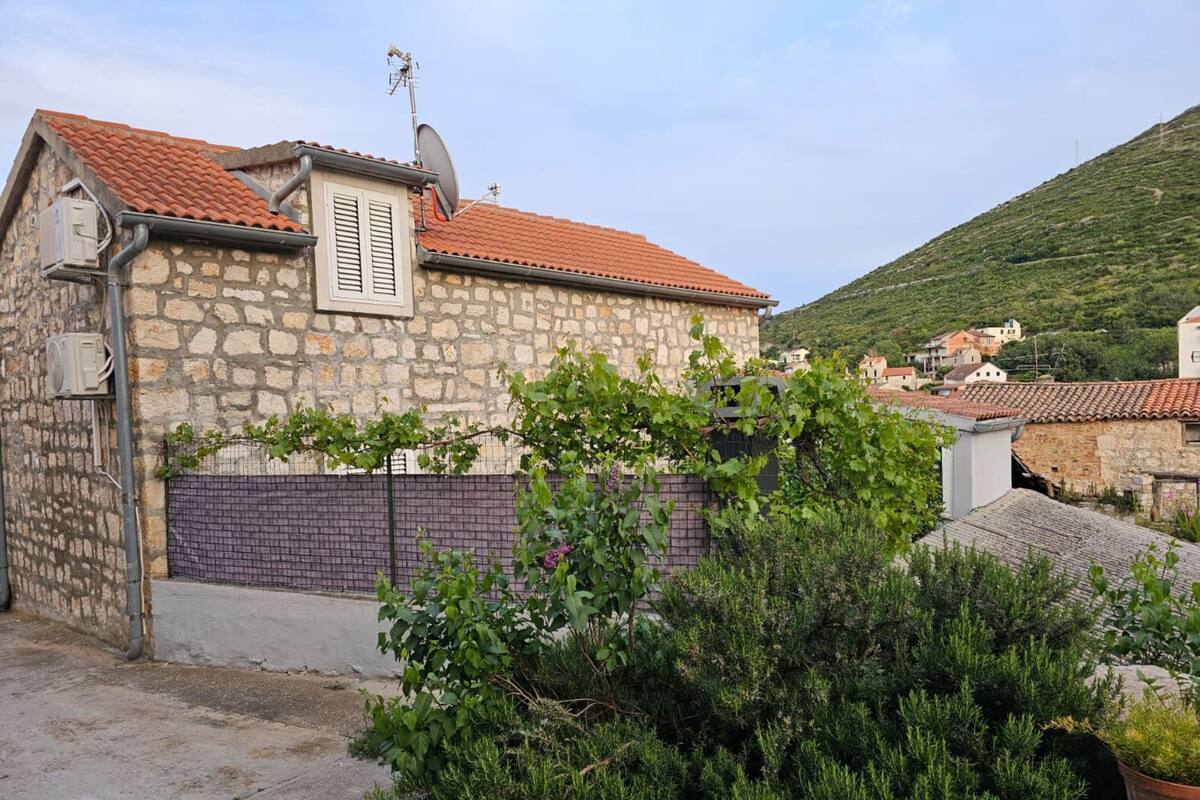 A stone building with a tiled roof, a satellite dish, and a fenced garden with shrubs.