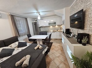 A compact living space with a bed, a dining table, a kitchen area, and a TV mounted on a stone wall. - Apartments Diadora (Vis)
