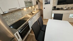 Une cuisine moderne avec des meubles blancs, un four encastré et un coin repas comprenant une table blanche et des chaises noires.