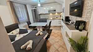 Une chambre d’hôtel compacte comprenant un lit, une petite table à manger, un coin cuisine et un téléviseur fixé au mur, qui est en pierre.