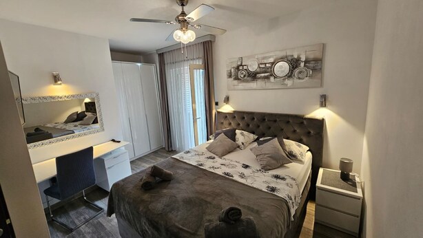 Une chambre à coucher comprenant un lit, une table de chevet, une commode, un bureau, une chaise, une armoire et un ventilateur de plafond.