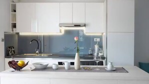 A modern kitchen with white cabinetry, a stainless steel range hood, and a central island with a vase and a wine glass. - Blue Magic Apartment (Seget)