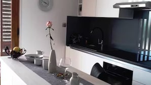 A modern kitchen with a black range hood, a clock on the wall, and a dining table with a vase and a bowl. - Blue Magic Apartment (Seget)