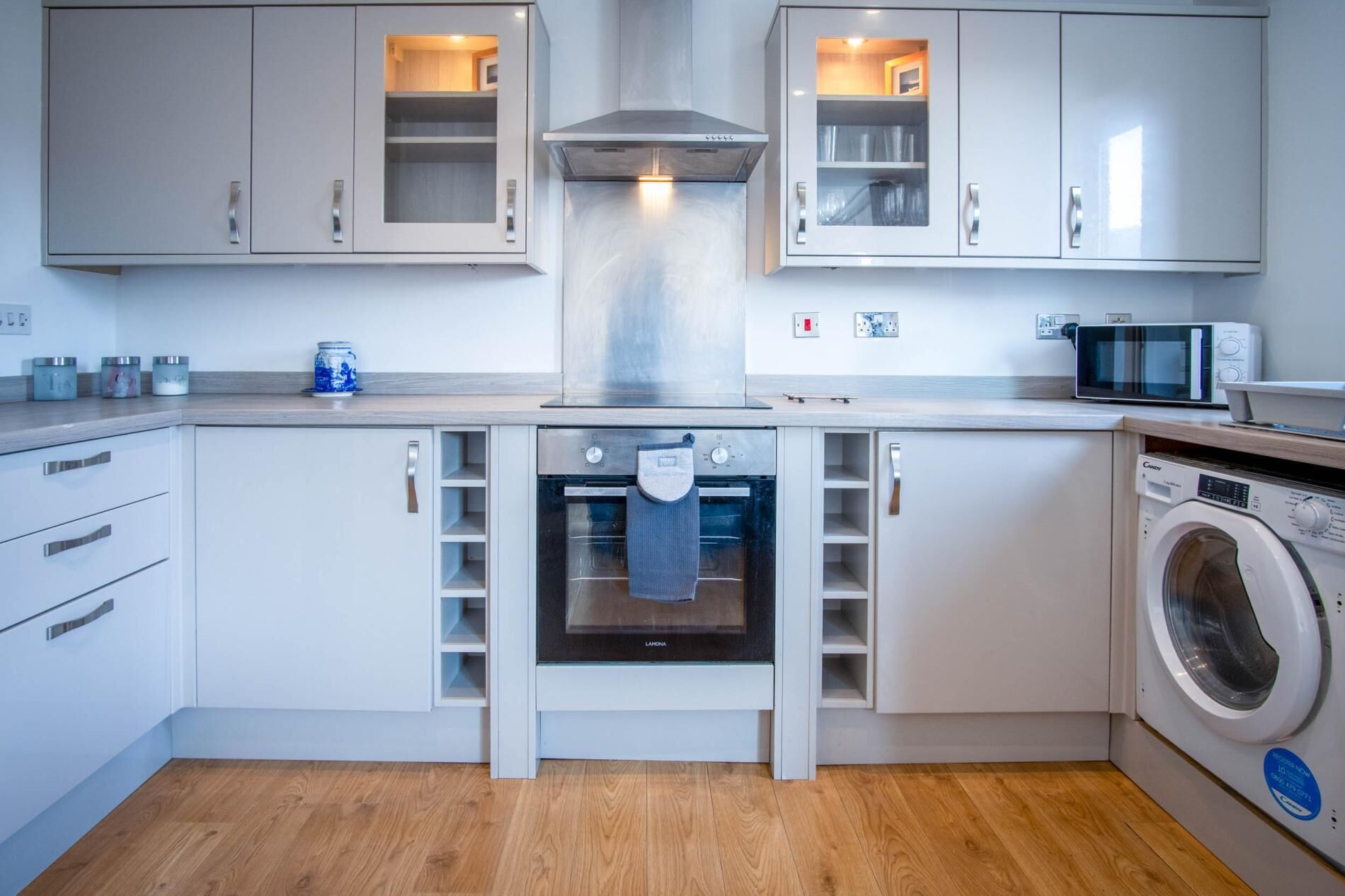 A modern kitchen with white cabinets, a built-in oven, a microwave, and a washing machine.