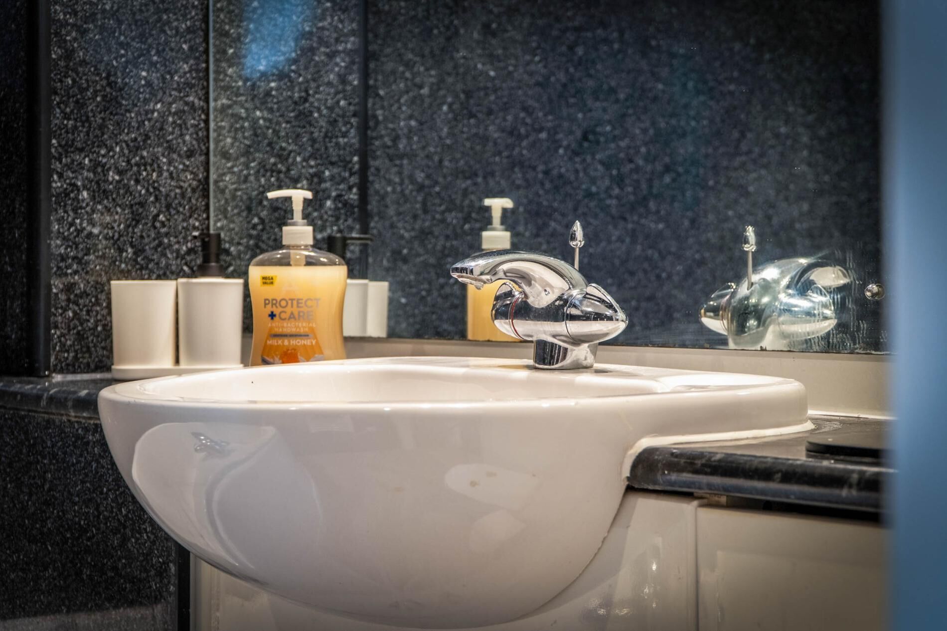 A bathroom with a white sink, a chrome faucet, and a bottle of soap.