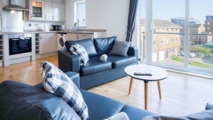 Un apartamento moderno con cocina, sofá, mesa de centro y un amplio ventanal con vistas a edificios.
