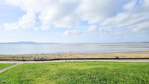 A coastal landscape with a grassy foreground, a sandy beach, and a calm sea under a partly cloudy sky. - Ocean View - 2 Bedroom Apt - Llanelli (Llanelli)