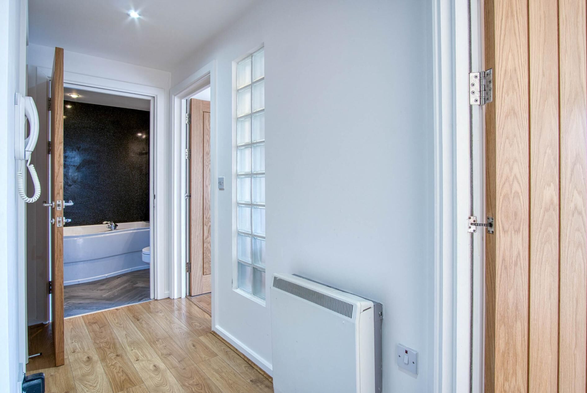 A hallway with a wooden floor, a white radiator, and a bathroom with a bathtub and toilet visible through an open door.