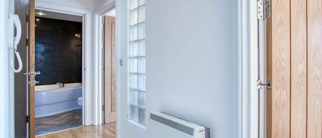 A hallway with a wooden floor, a white radiator, and a bathroom with a bathtub and toilet visible through an open door.