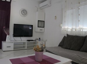 A living room with a flat-screen TV, a clock, an air conditioner, and a window with blinds. - Holiday Home Nadalina (Vodice)