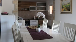 En matplats med ett vitt bord, stolar, en vas med blommor och ett kök i bakgrunden.