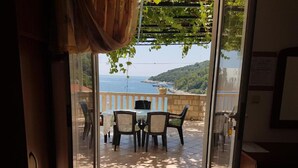 A room with a sliding glass door leading to an outdoor patio with a table and chairs, a pergola with hanging plants, and a view of the sea and hills. - Villa Azure Saplunara (Mljet)