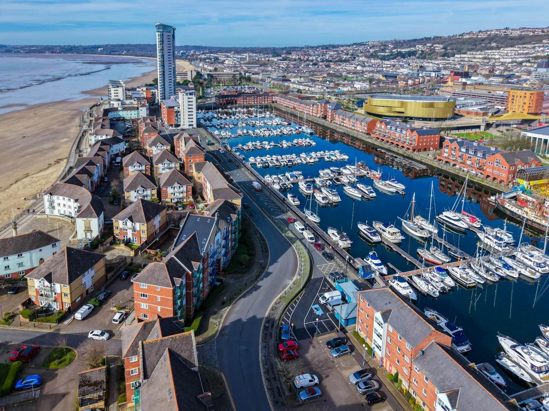 A marina with numerous boats docked, a curved road, and residential buildings with red and white facades.