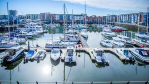 A marina with numerous boats docked, a clear sky, and buildings in the background. - The Crows Nest - 1 Bed Apartment - Swansea Marina (Swansea)