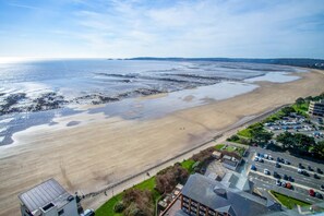 Une vue sur la côte, avec une plage de sable, un parking et des bâtiments dotés de toits plats.