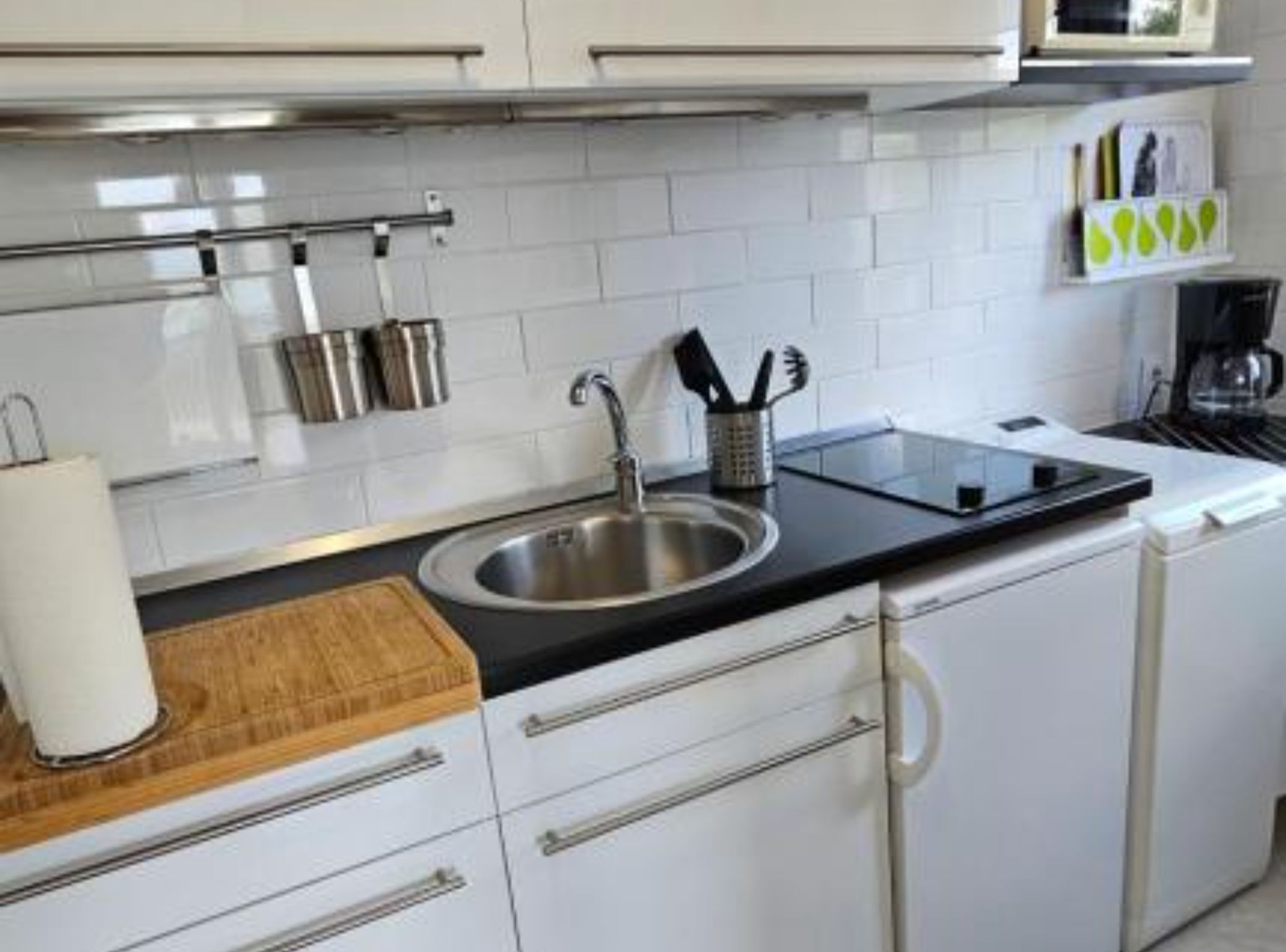 A modern kitchen with a stainless steel sink, white cabinets, a black countertop, and a coffee maker.