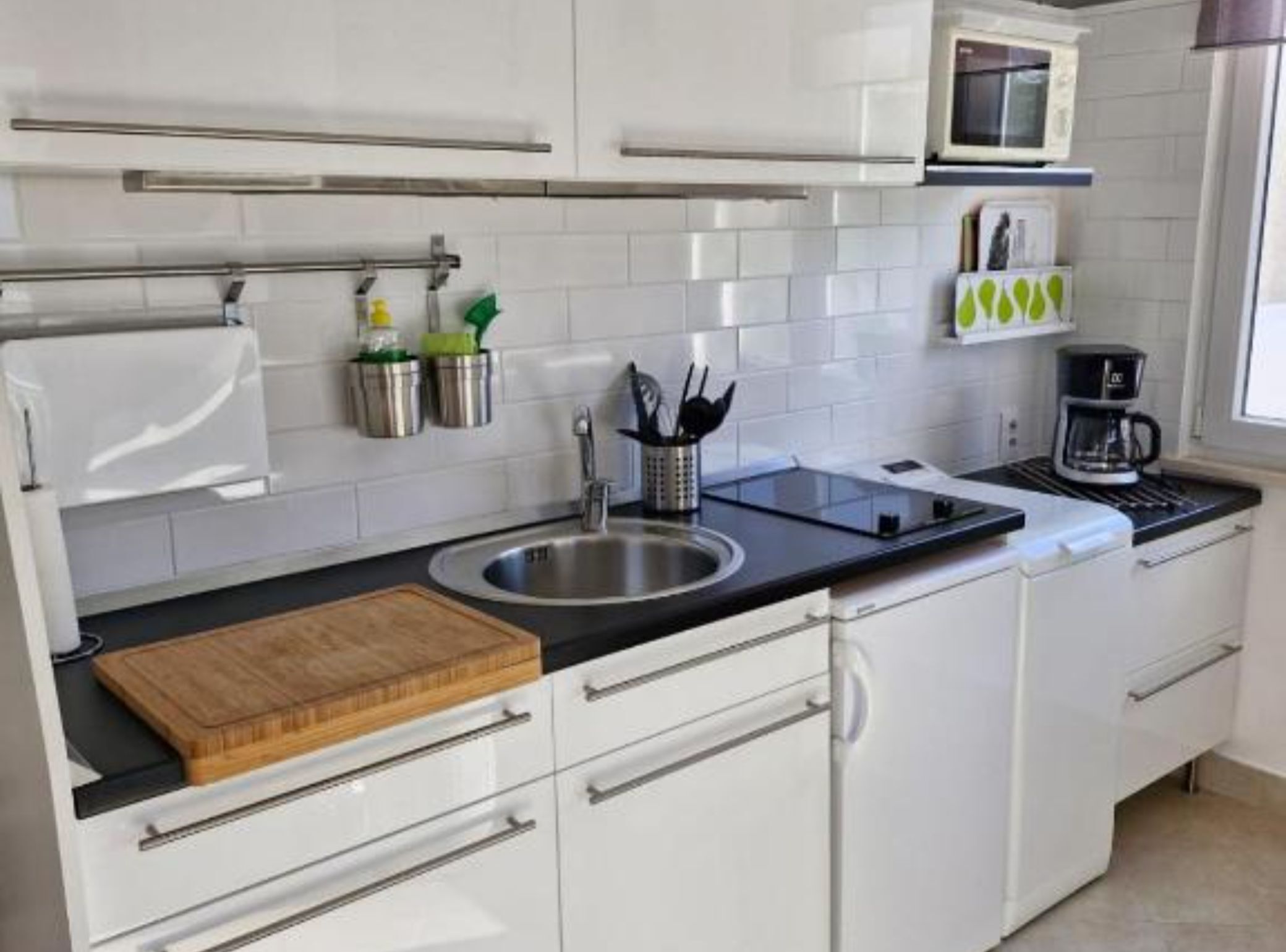 A modern kitchen with white cabinets, a stainless steel sink, a microwave, and a coffee maker.