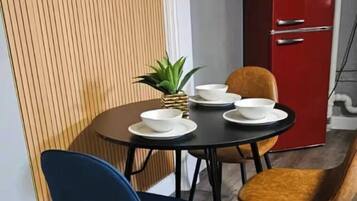 Un coin repas avec une table dressée pour quatre personnes, deux chaises bleues, deux chaises orange et un buffet rouge en arrière-plan.