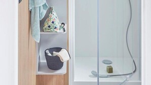 Un baño con cabina de ducha de vidrio, un perchero y repisas con artículos de aseo.