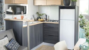 Una kitchenette compacta con microondas, estufa y refrigerador. Hay una zona de comedor con mesa y sillas, y un sofá con cojines.