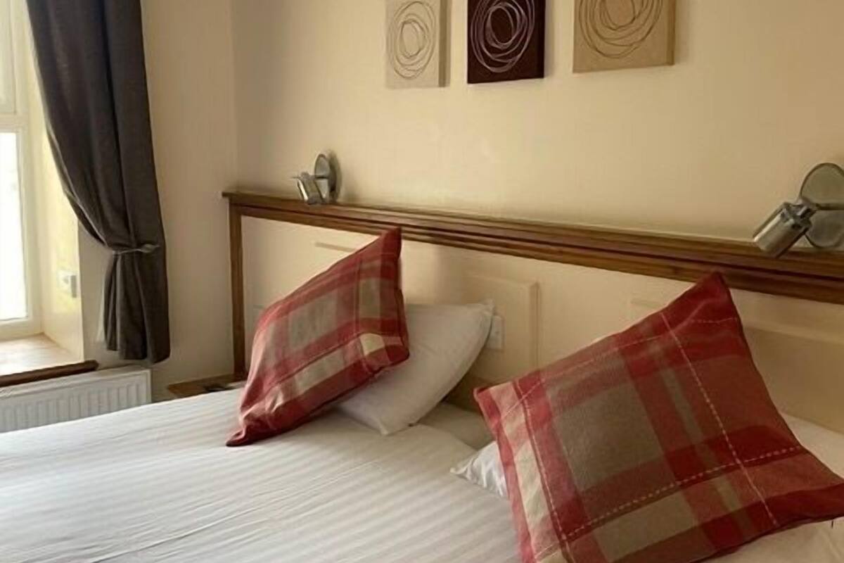 Hotelkamer met een bed, twee kussens, een hoofdbord, een raam met gordijnen en drie kunstwerken aan de muur.