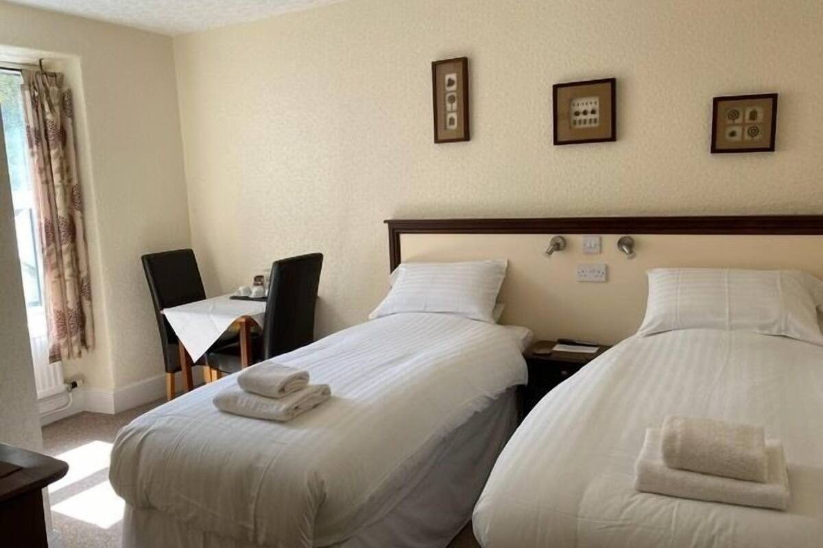 Een hotelkamer met twee bedden, een klein tafeltje, een stoel en een raam met gordijnen.