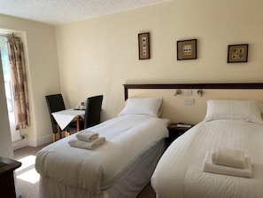 A hotel room with two beds, a small table, a chair, and a window with curtains.