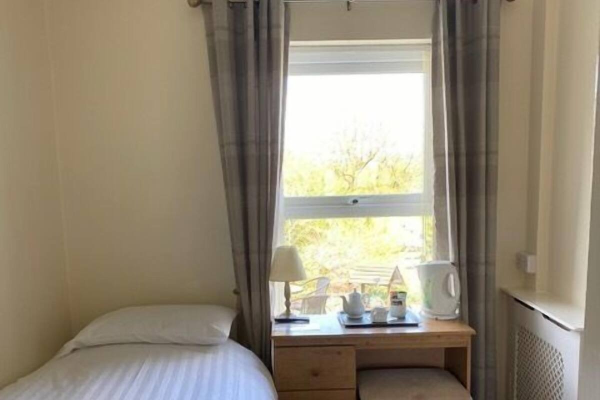 Een slaapkamer met een bed, een bureau met stoel, een radiator en een raam met gordijnen.