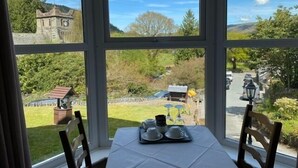 A table with a tray of cups and saucers, a chair, and a view of a rural landscape with a stone building and greenery. - Church hill house (Betws-Y-Coed)