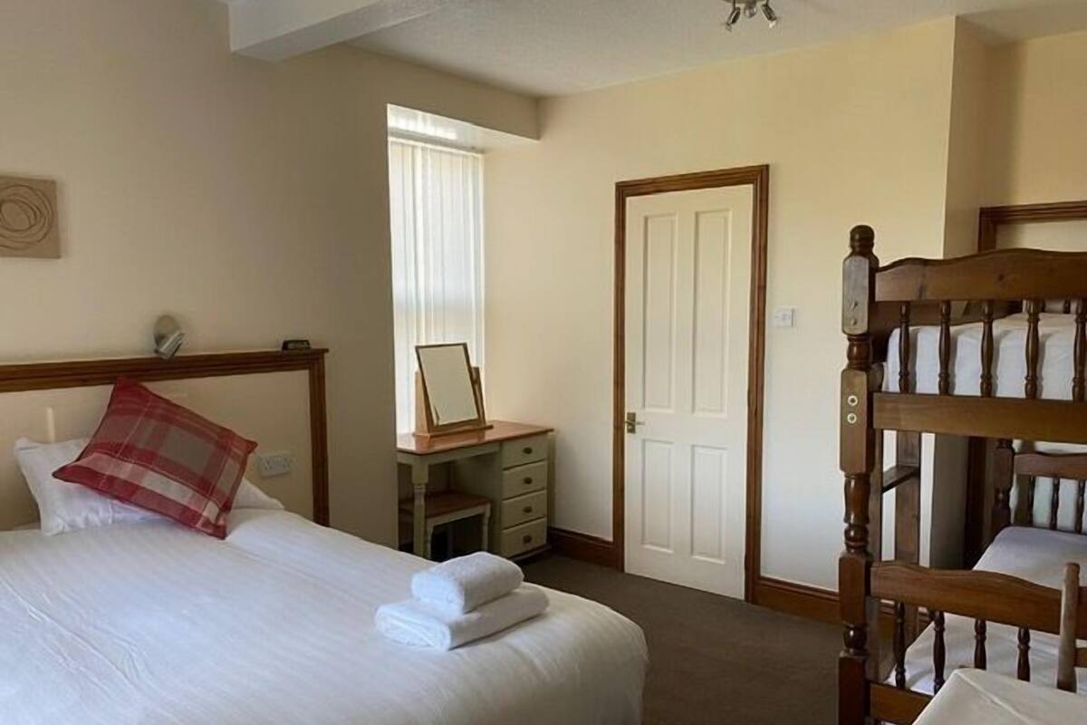 Een hotelkamer met een bed, een bureau, een spiegel, een deur en een stapelbed.