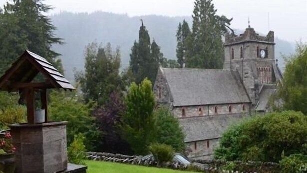 A historic building with a clock tower, surrounded by lush greenery and a stone structure. - Church hill house (Betws-Y-Coed)
