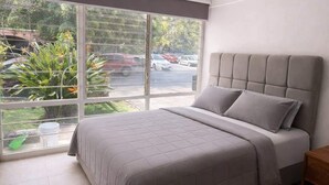 A bedroom with a large window, a bed with grey bedding, and a nightstand. - Private Apartment, Milan Providencia (Guadalajara)