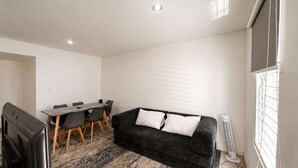 A room with a dark sofa, a dining table with chairs, and a standing heater. - Private Apartment, Milan Providencia (Guadalajara)