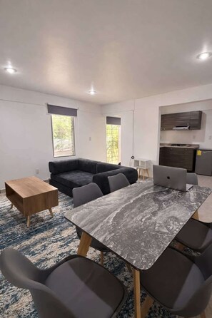 Ein modernes Wohnzimmer mit einem dunklen Sofa, einem Holztisch und einem Esstisch aus Marmor mit Stühlen.