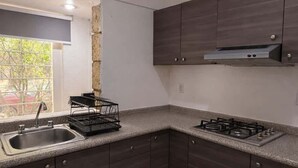 A modern kitchen with dark cabinetry, a gas stove, a sink, and a window with a view of greenery. - Private Apartment, Milan Providencia (Guadalajara)