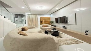 Een moderne woonkamer met een gebogen bank, een salontafel en een flatscreen televisie aan de muur.