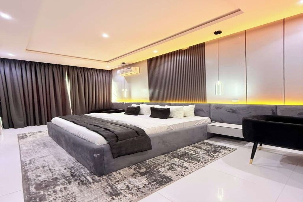A modern bedroom with a large bed, a bedside table, a sofa, and a wall-mounted TV.